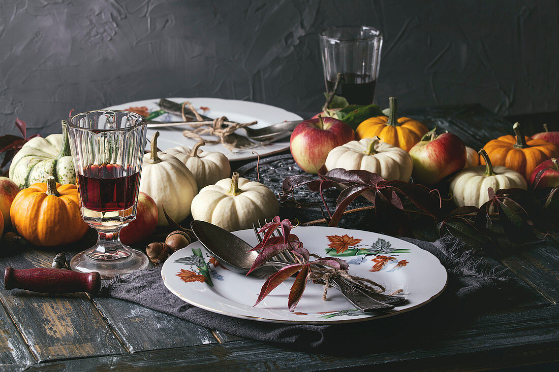 Autumn holiday table decoration setting with decorative pumpkins, apples, red leaves, empty plate with vintage cutlery