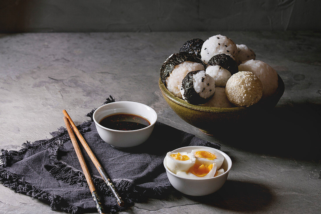 Bowl with different size rice balls with black sesame and seaweed nori, served with soft boiled eggs, soy sauce