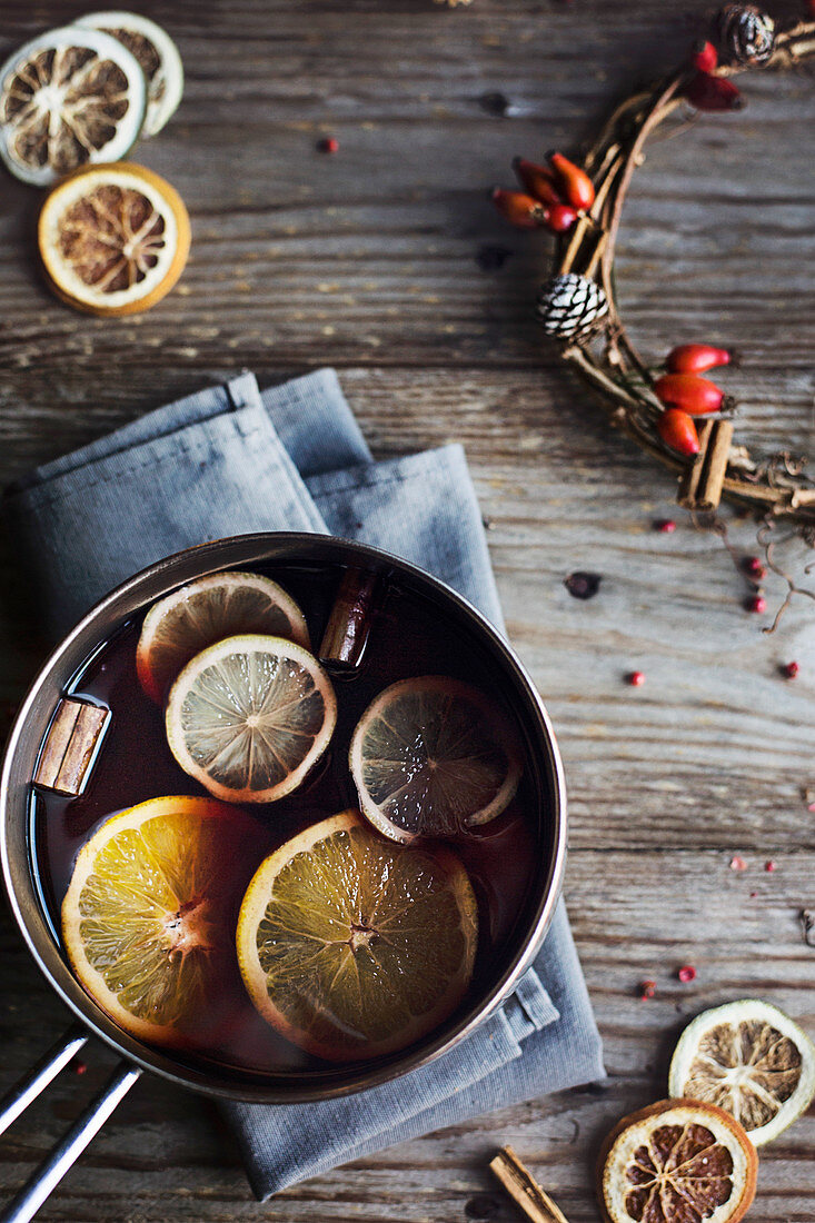 Hot winter drink. Mulled wine with orange, lemon and spices in a casserole on wooden rustic table