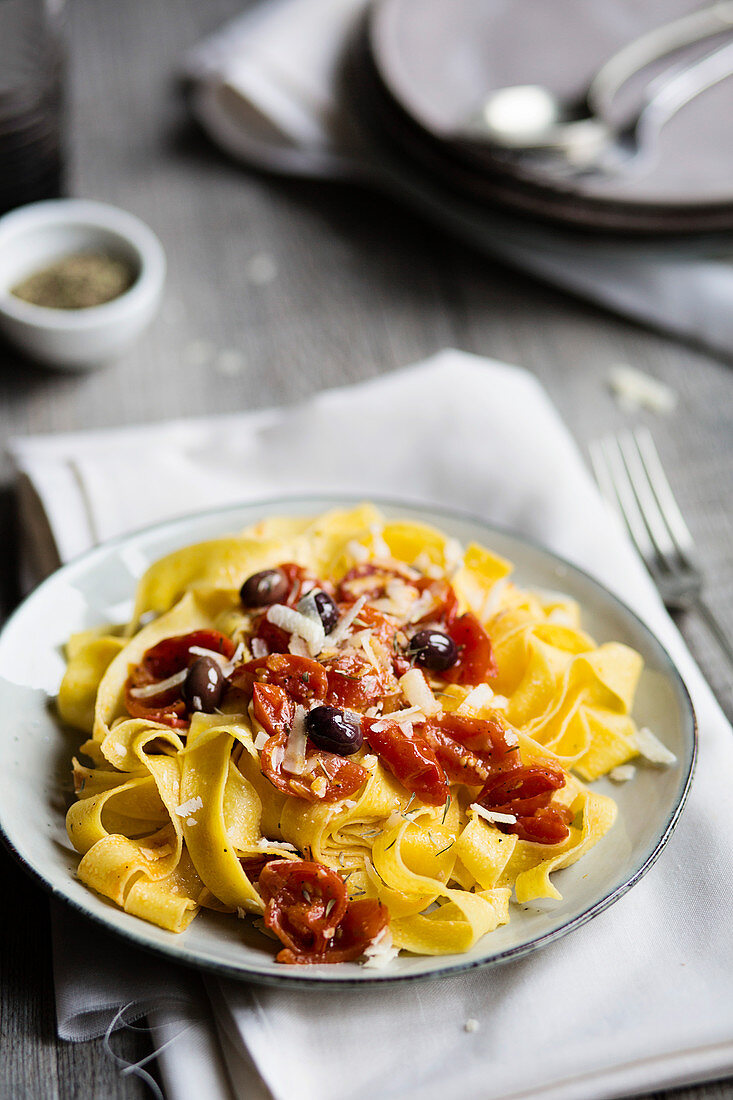 A typical italian dish pappardelle pasta with tomato sauce, olives and parmesan on wooden table