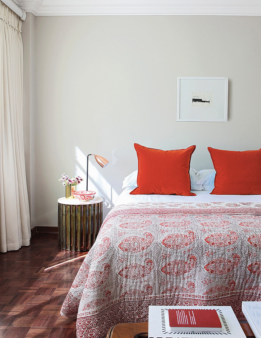 Doppelbett mit rot gemusterter Tagesdecke und roten Kissen in hellem Schlafzimmer
