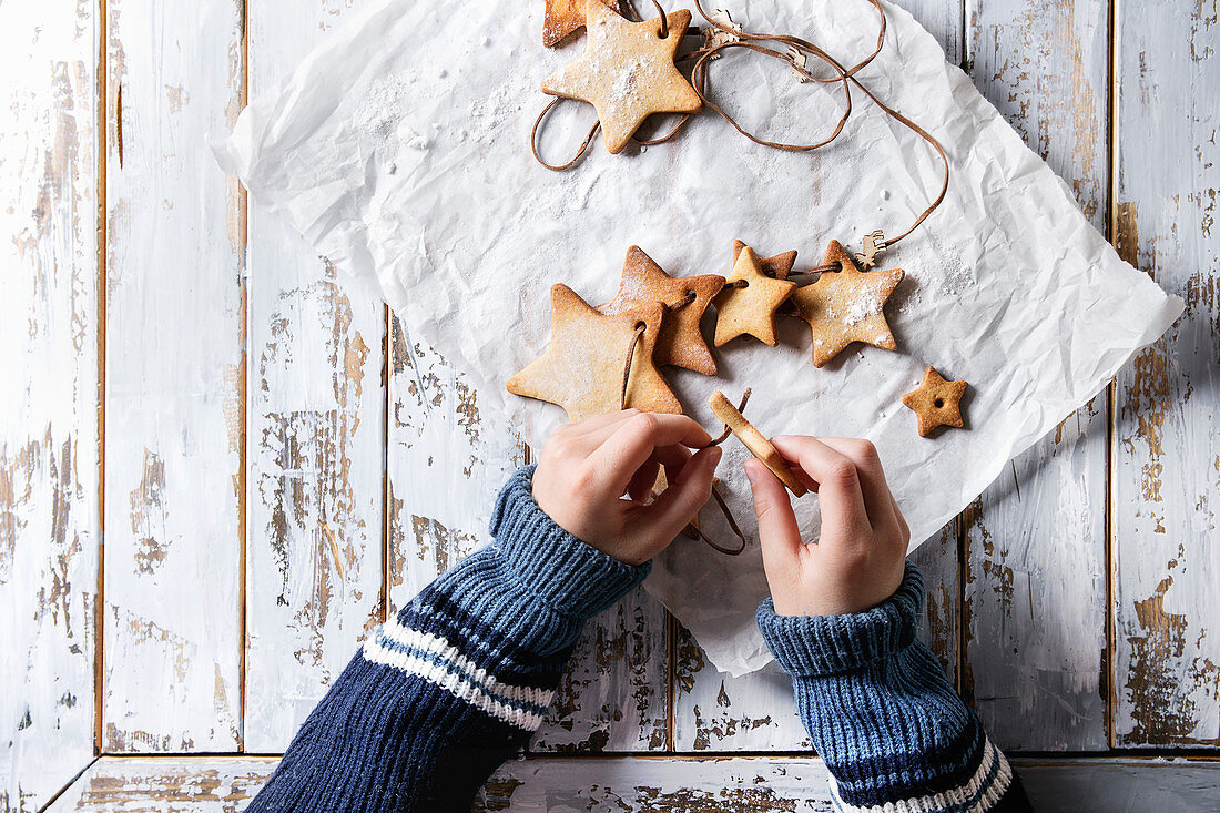 Child hands make garland of homemade shortbread star shape sugar cookies