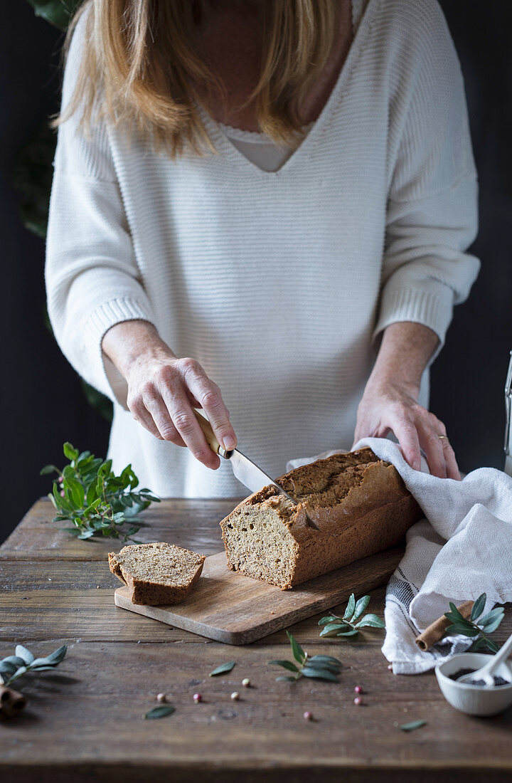 Frau schneidet selbstgebackenes Brot auf Holzbrett in Küche