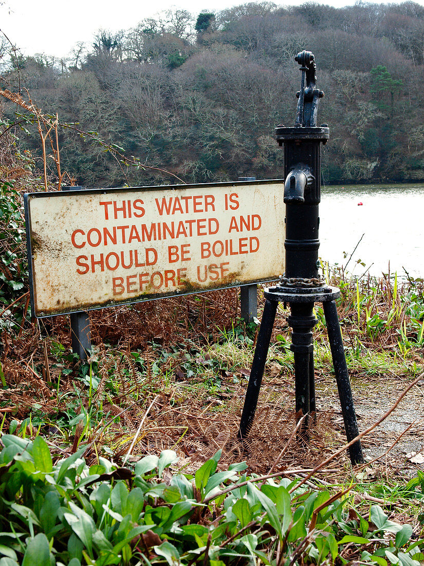 Contaminated water sign next to public water hand pump, Corn