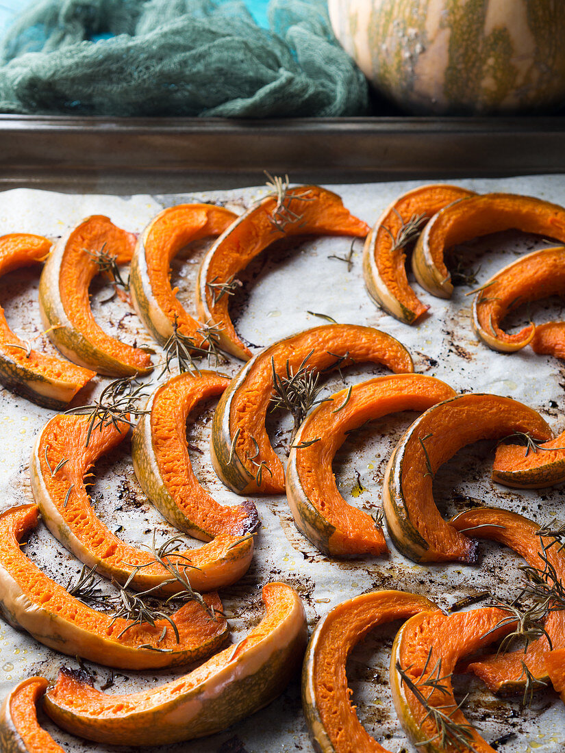 Baked pumpkin slices on baking parchment with rosemary