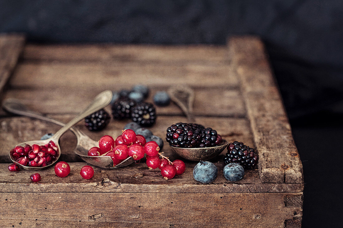 Rote Johannisbeeren, Granatapfelkerne, Blaubeeren und Brombeeren auf Holzkiste