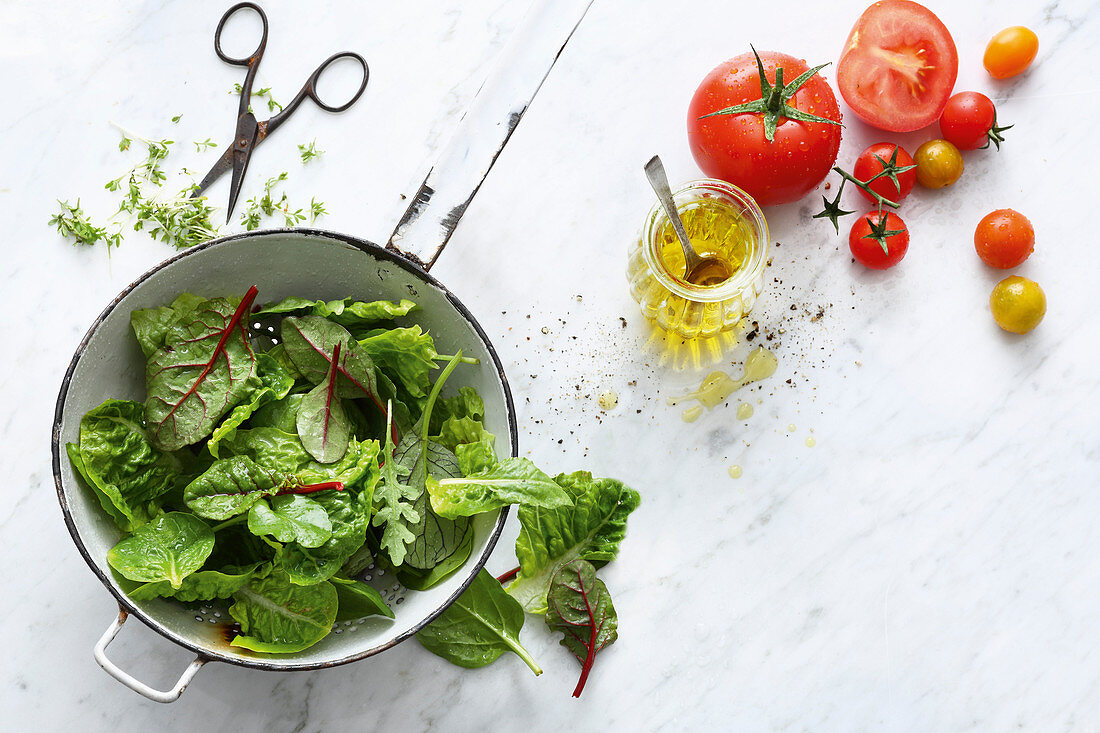 Frische Blattsalate im Sieb, Olivenöl und frische Tomaten