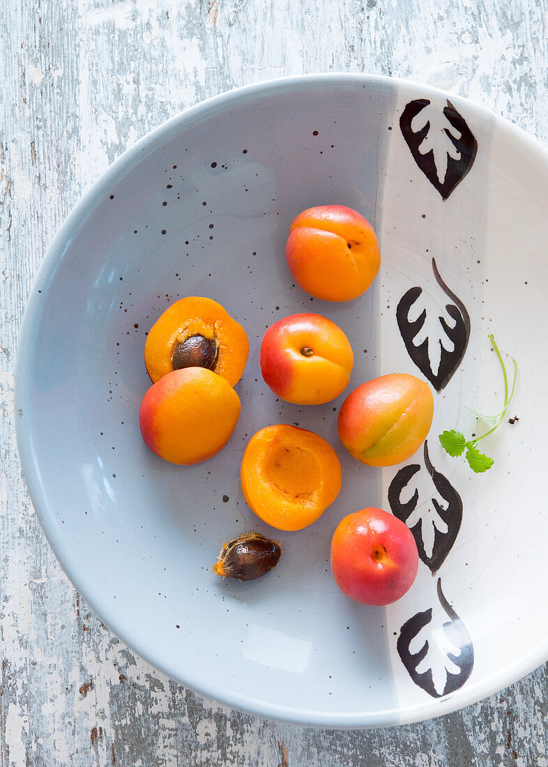 Fresh apricots, whole and halved, on a ceramic plate
