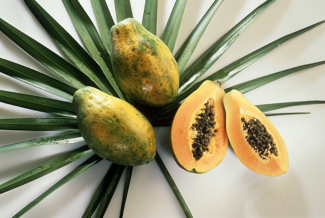 Two Whole Papayas and a Halved Papaya on Palm Leaves