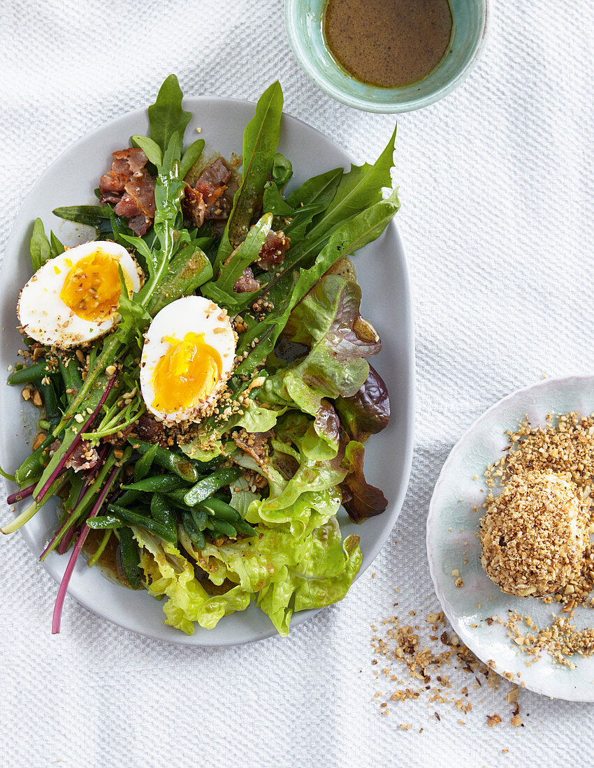 Soft boiled eggs coated in nuts, on a salad with bacon