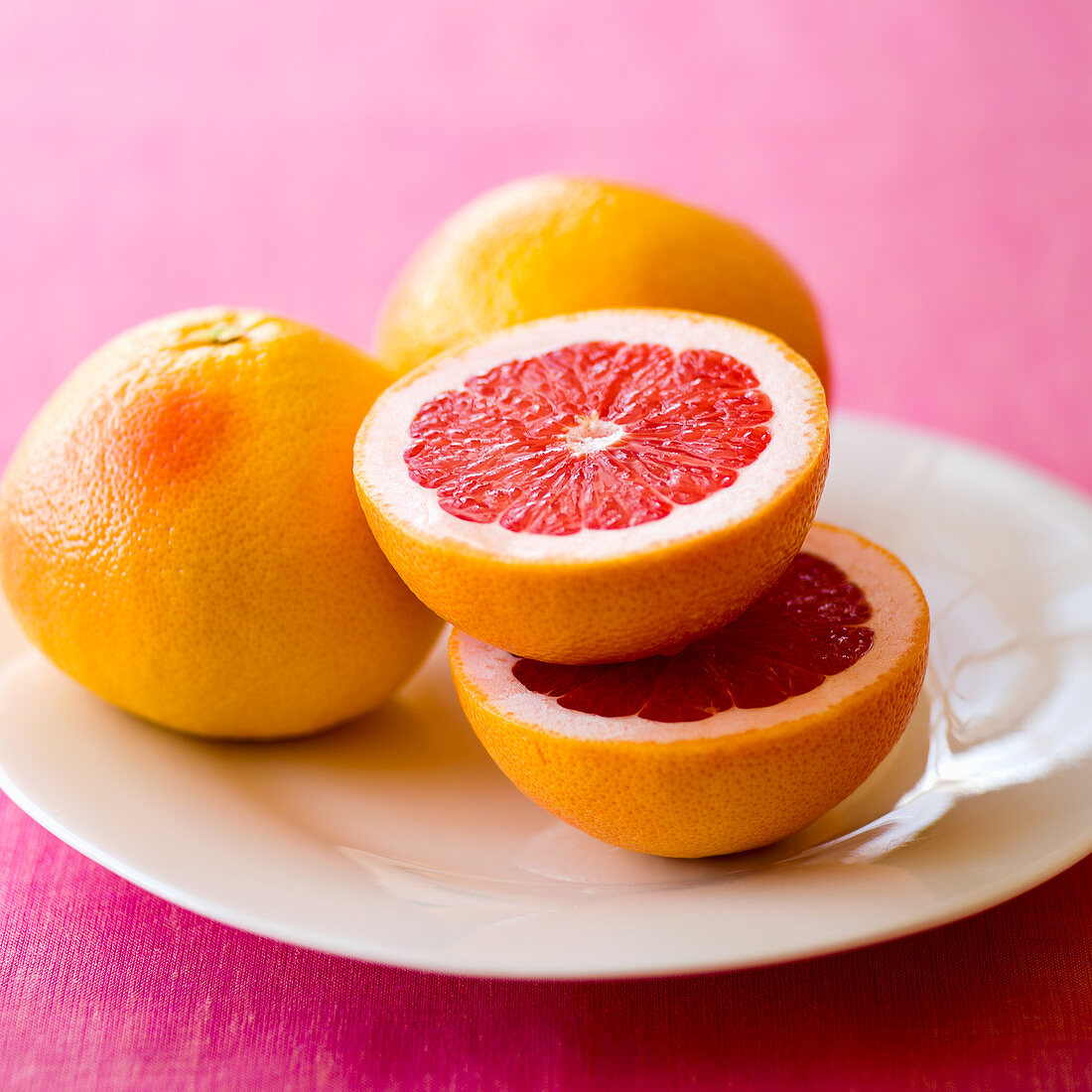 Rosa Grapefruits, ganz und halbiert, auf Teller