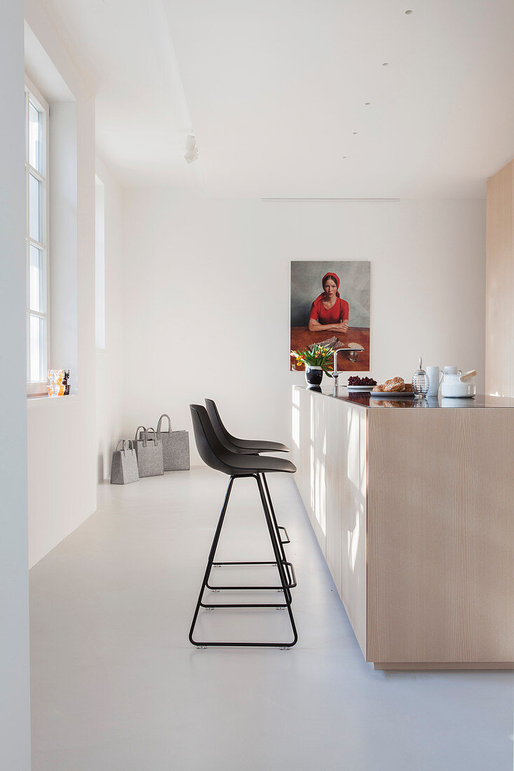 Black bar stools at pale wooden island counter in bright kitchen