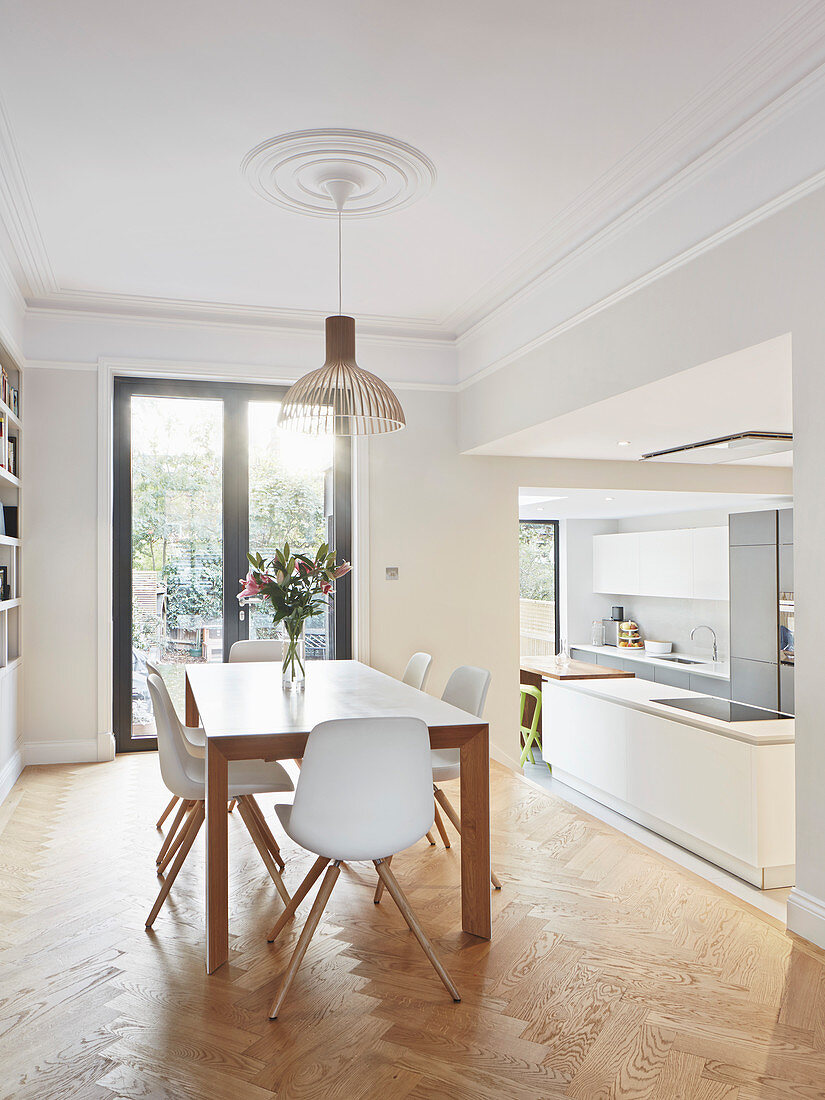 White chairs around dining table in front of open doorway leading into open-plan kitchen