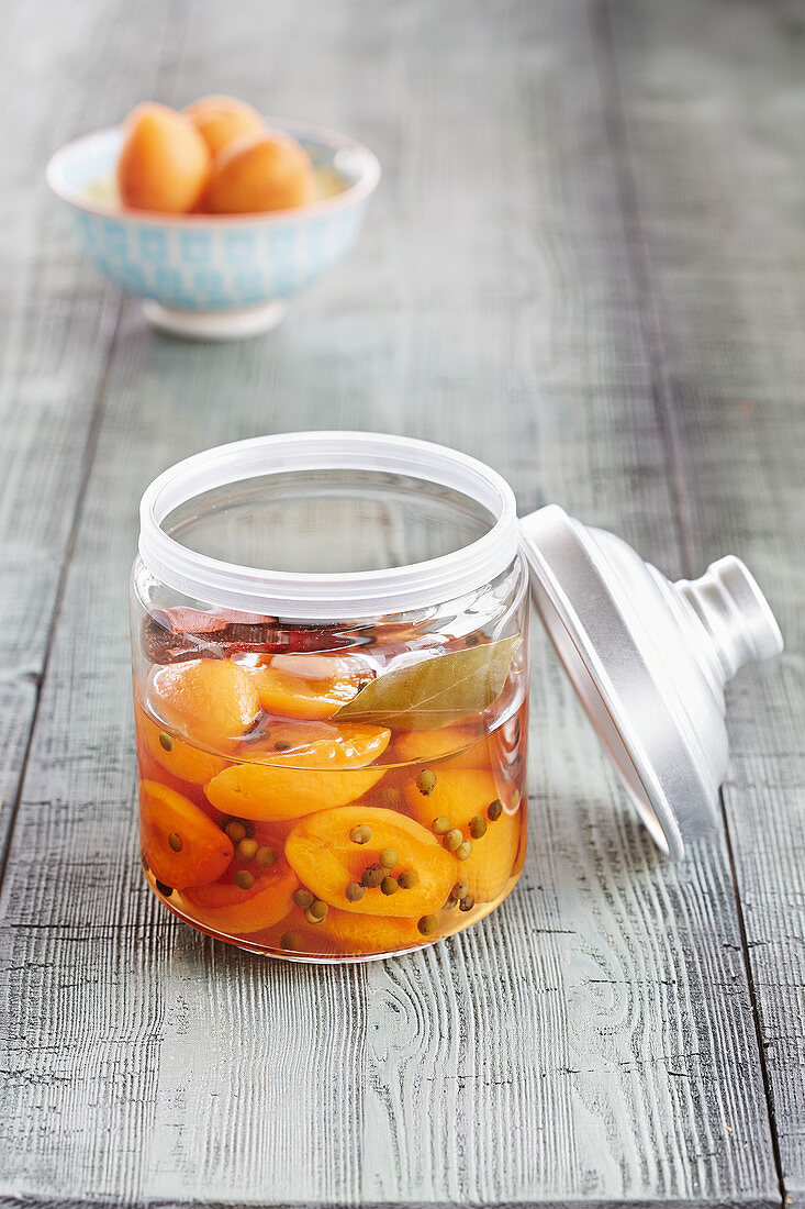 A jar of preserved apricots with peppercorns