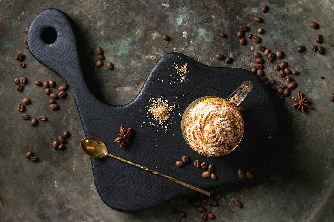 Glass of spicy pumpkin latte with whipped cream and cinnamon standing on black serving board