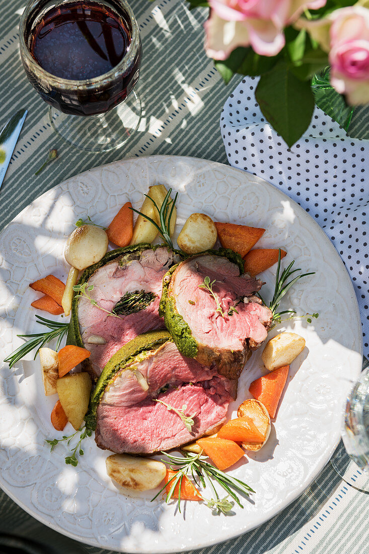 Lamb with a herb crust and vegetables on a summery table outdoors