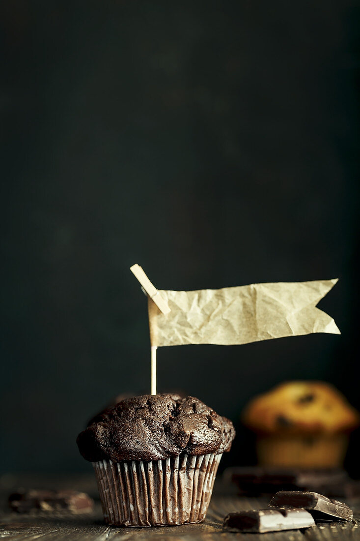 Schokoladenmuffins mit Papierfähnchen vor dunklem Hintergrund