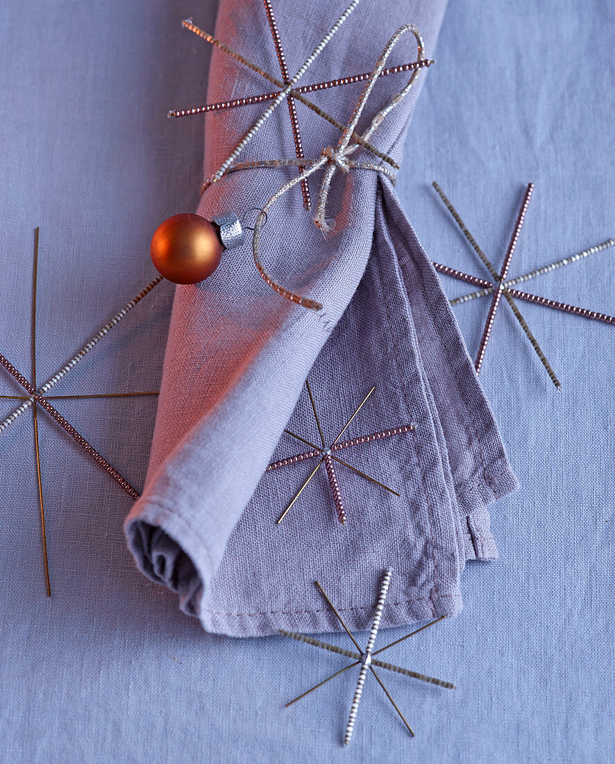 Christmas arrangement of linen napkin, silver stars and copper-coloured bauble