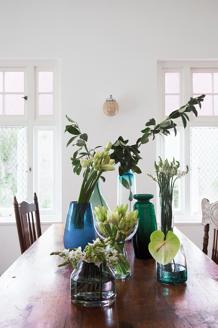 Glass vases of flowers and leafy branches on rustic dining table