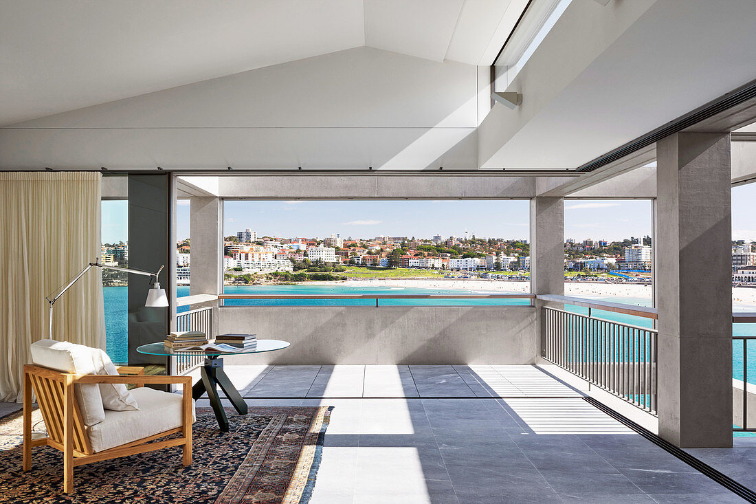 Designer armchair, standard lamp and round table on covered terrace with sea view