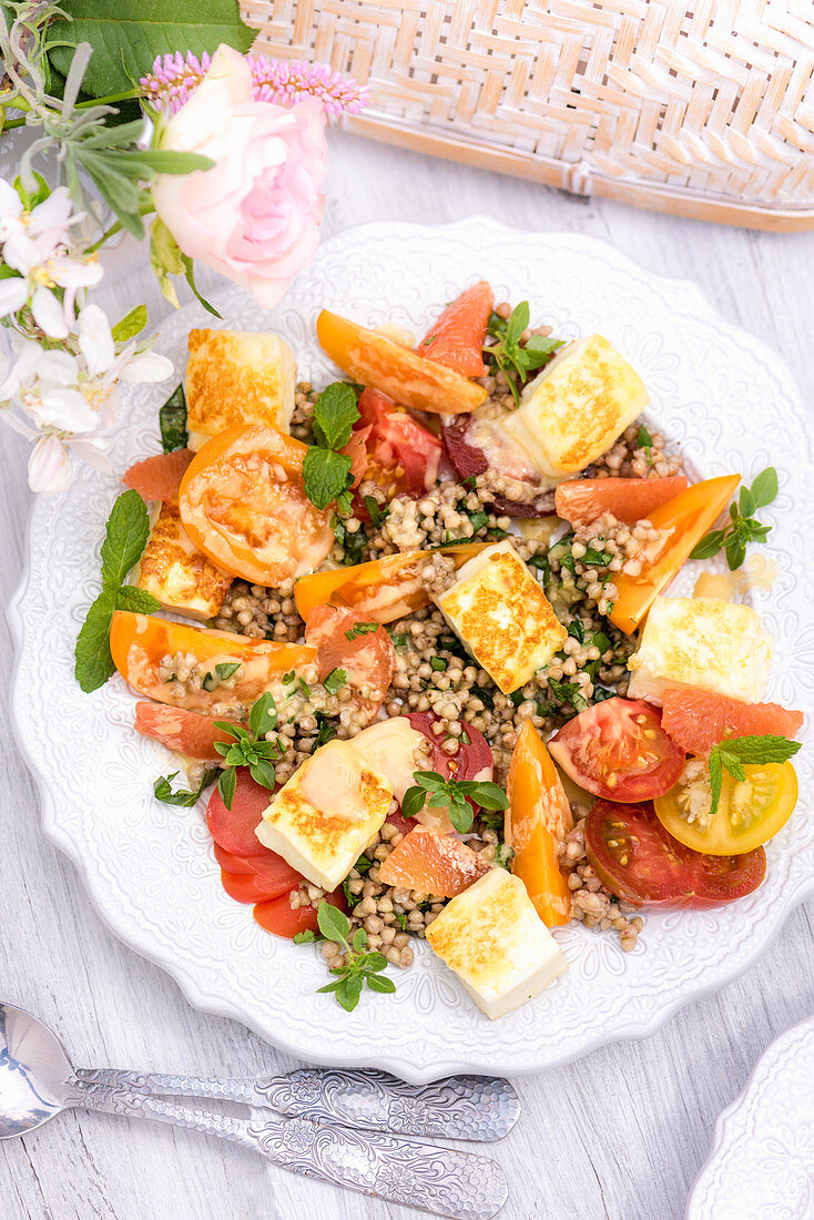 Summer buckwheat salad with tomatoes and halloumi on a table outside