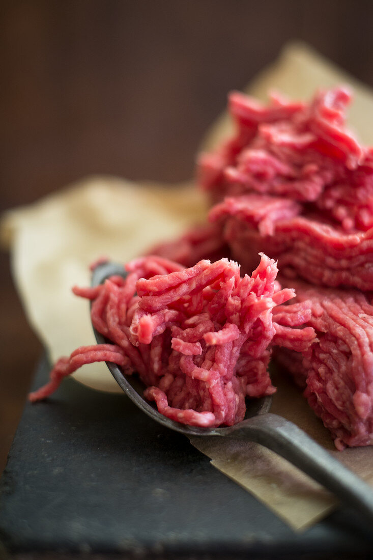 Frisches Rinderhackfleisch mit Löffel auf Papier (Nahaufnahme)