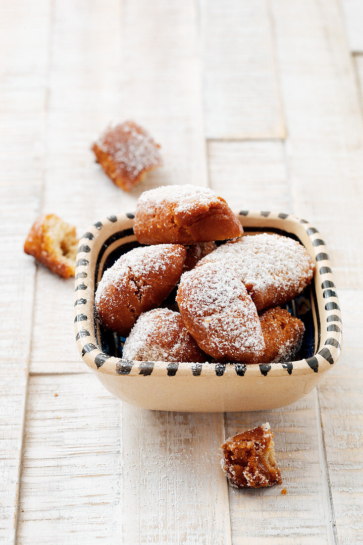 A bowl of homemade, deep-fried pastries with icing sugar