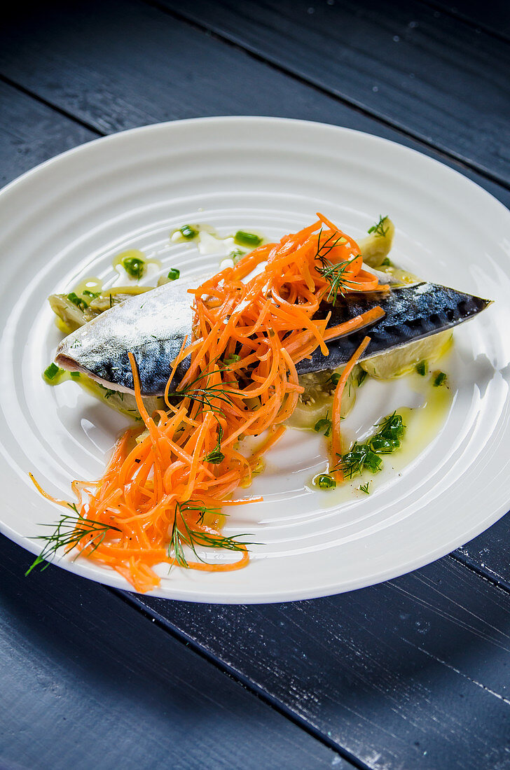 Blue mackerel fish fillet with aubergines and carrots drizzled with olive oil and garnished with dill and herbs on a white plate