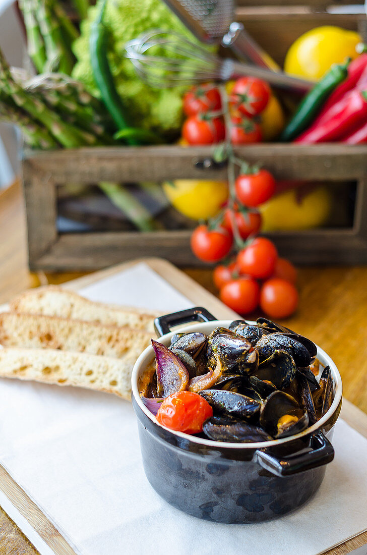 Fresh mussels in a white wine and tomato sauce with red onions and cherry tomatoes in a pot