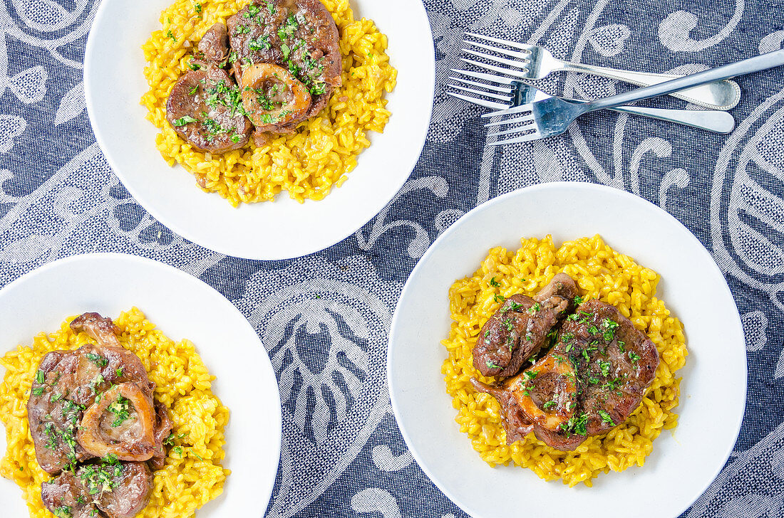 Three portions of osso buco milanese meat on a yellow saffron risotto garnished with fresh chopped parsley