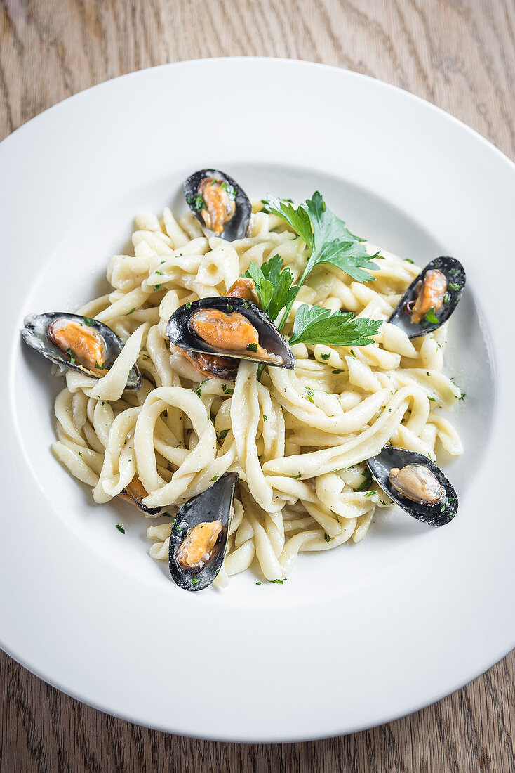 Traditional artisanal homemade fresh pasta with mussels and a creamy pecorino cheese sauce garnished with parsley in a white plate