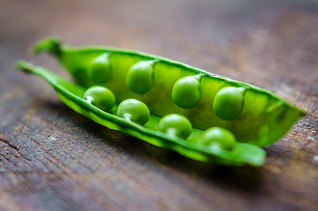 Close up of fresh green peas in a pod on a dark wooden background