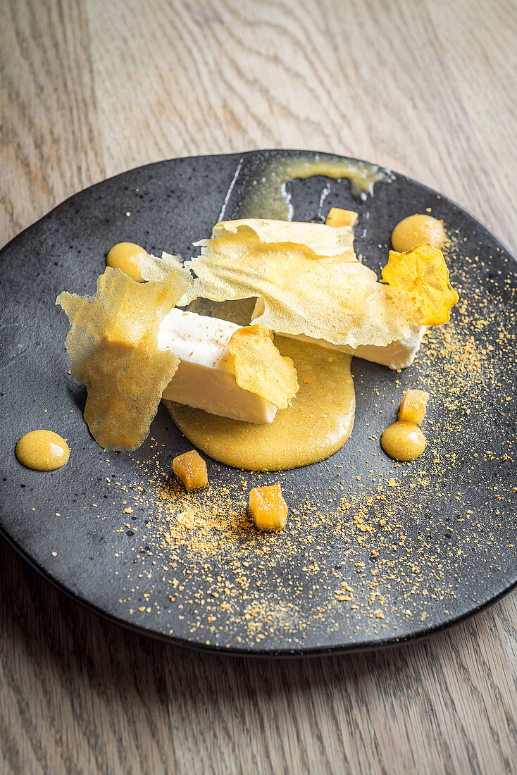 Persimon cheesecake with a persimon puree and crisps on a black plate and light wooden background