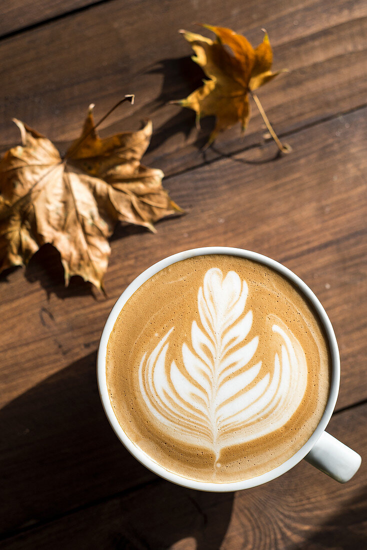 Flat white, cappuccino coffee with rosetta or florette latte art on a wooden background with autumn leaves