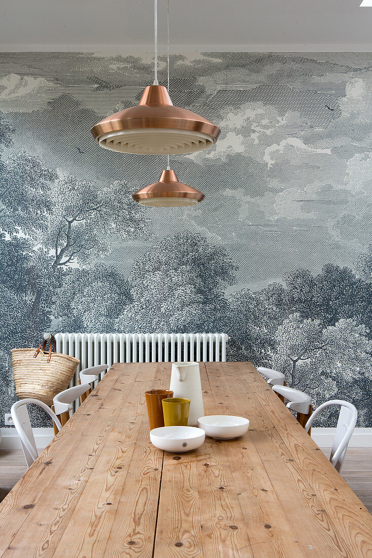 Long wooden table and chairs in front of mural wallpaper