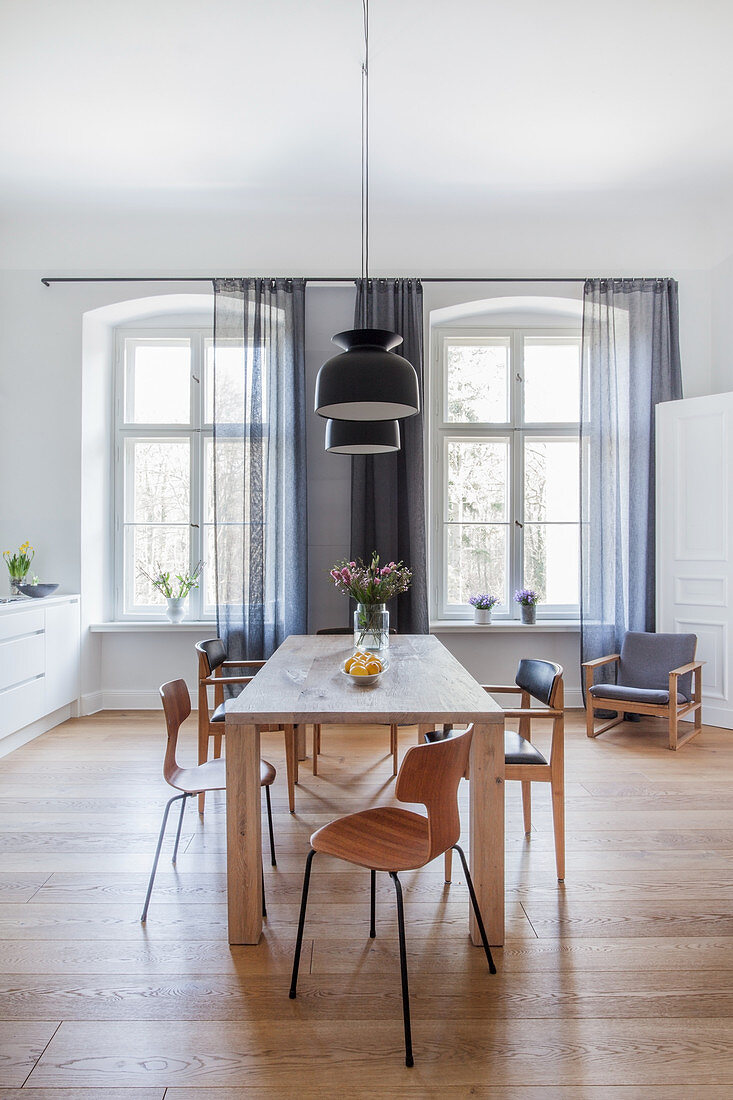 Designer chairs around wooden table in dining room with two period windows