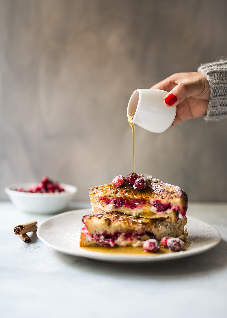 Frau giesst Sirup über French Toast mit Cranbeeries und Tvorog-Frischkäse