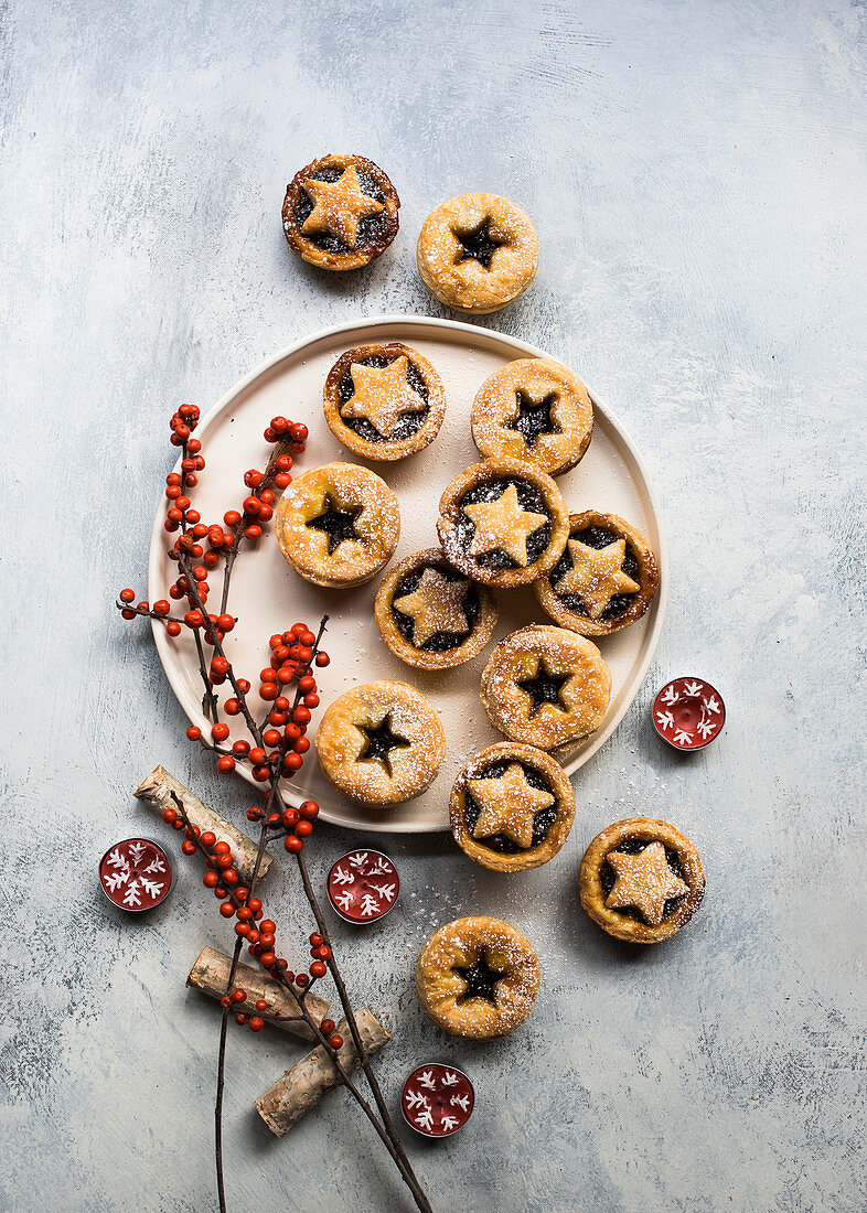 Small Christmas mince pies decorated with berry branches and tealights