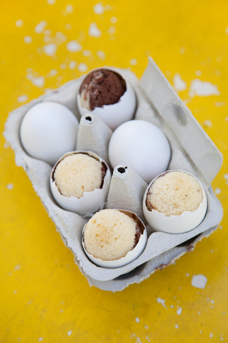 Cakes baked in egg shells in egg box on yellow surface