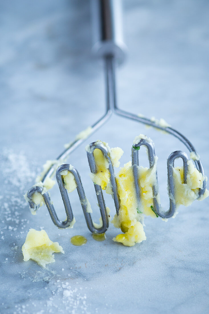 A potato masher with remnants of mash