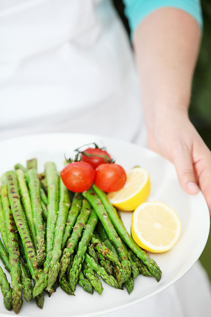 A woman holding a plate of grilled green asparagus