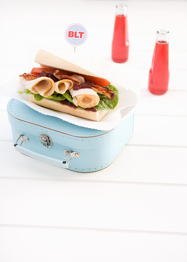 A BLT sandwich with sliced turkey breast on a vintage suitcase