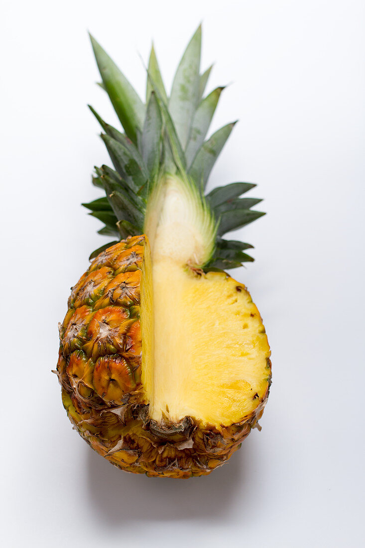 A pineapple on a white surface, with a quarter cut away