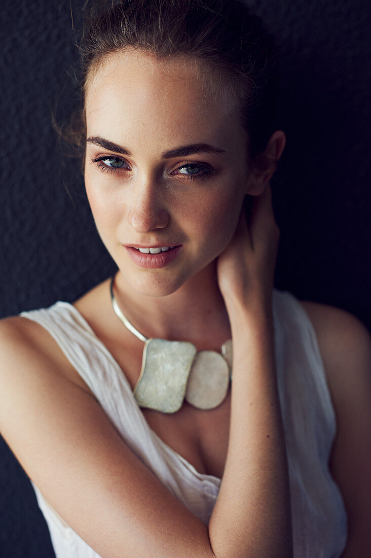 A young brunette woman wearing a white top and a chunky necklace