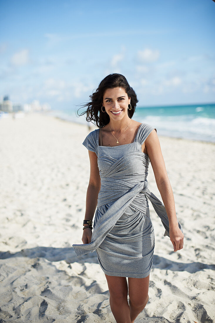 A young woman on a beach wearing a grey, wraparound dress