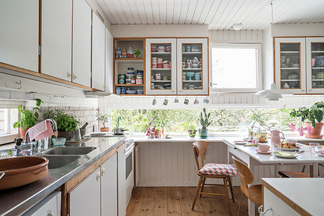 Ribbon windows along two walls in cosy, white kitchen-dining room