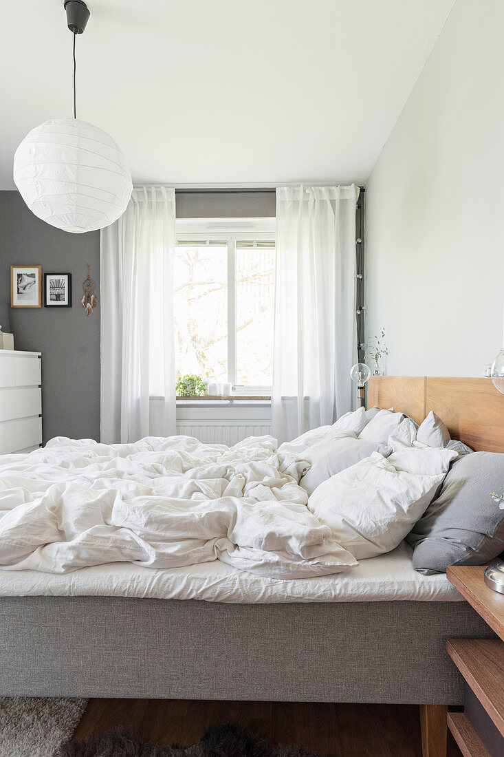 Unmade double bed with wooden headboard and light-bulb lamps on bedside tables