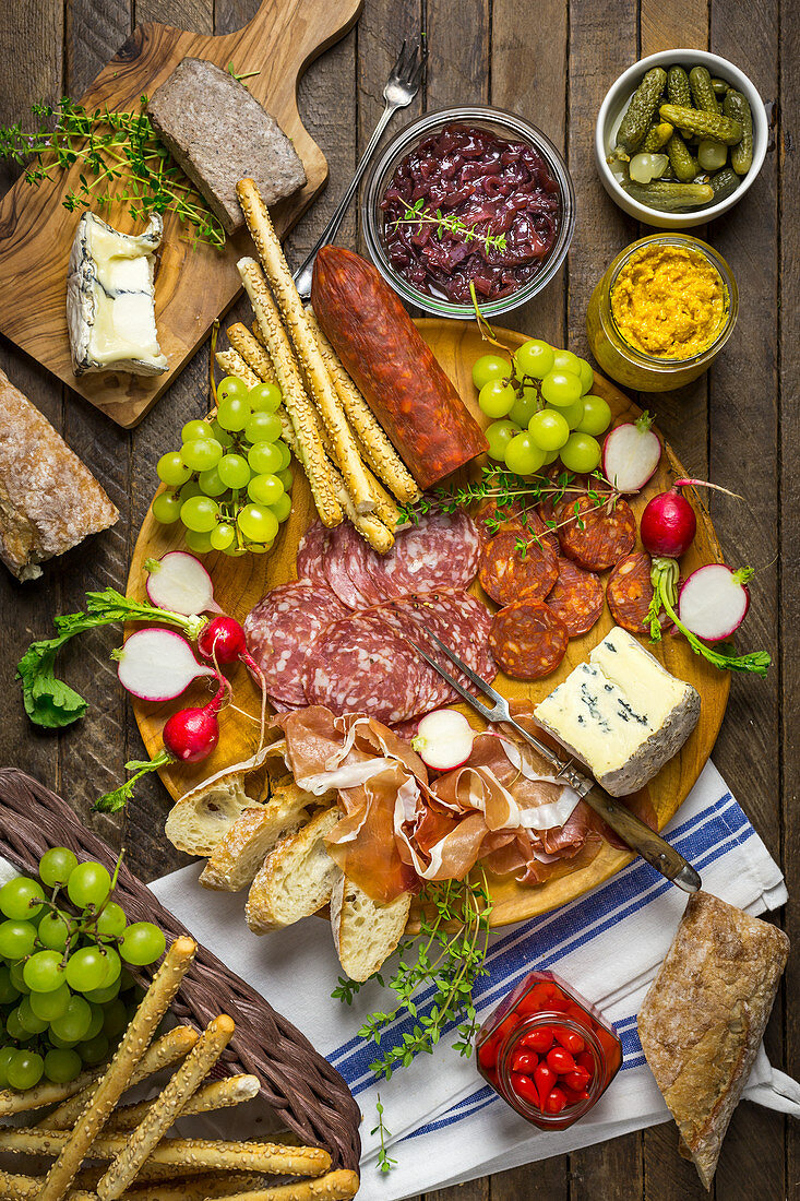 A snack platter with sausages, cheese, bread, grapes and pickles