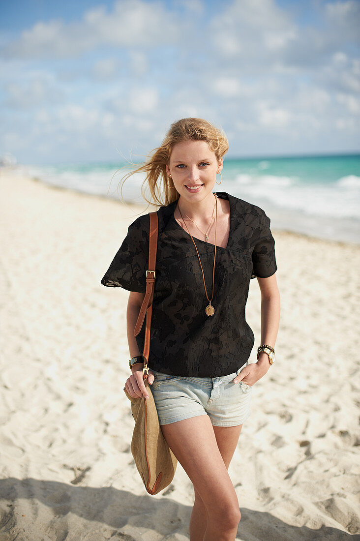 A blonde woman on a beach wearing a brown blouse and shorts