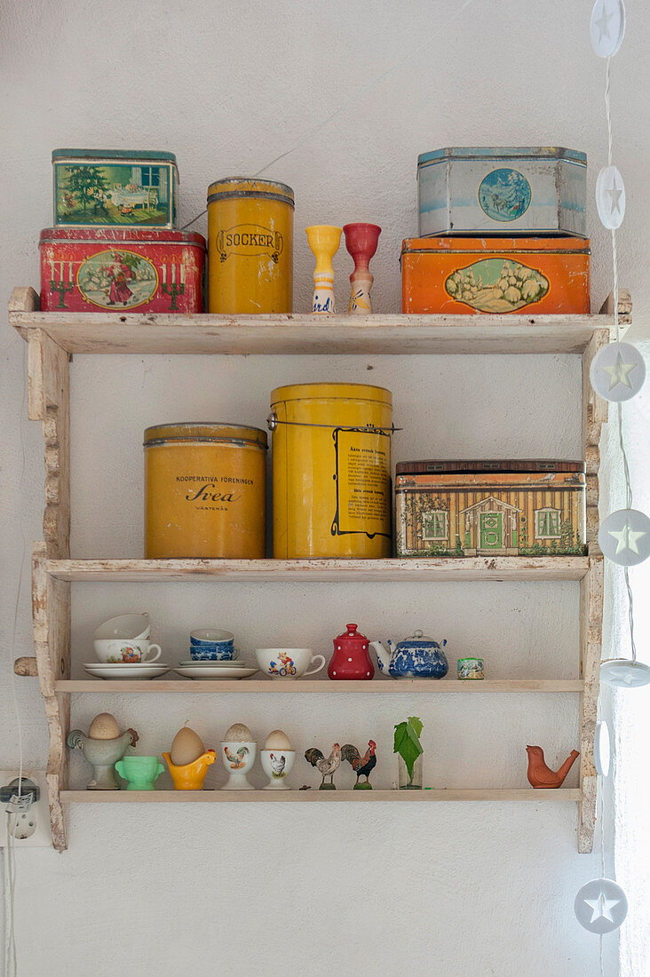 Brightly coloured tins and doll's crockery on old wall-mounted shelves